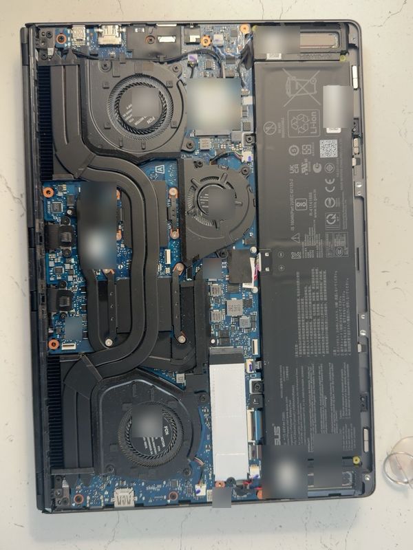 The same laptop opened up, showing three cooling fans and heatpipes across the motherboard